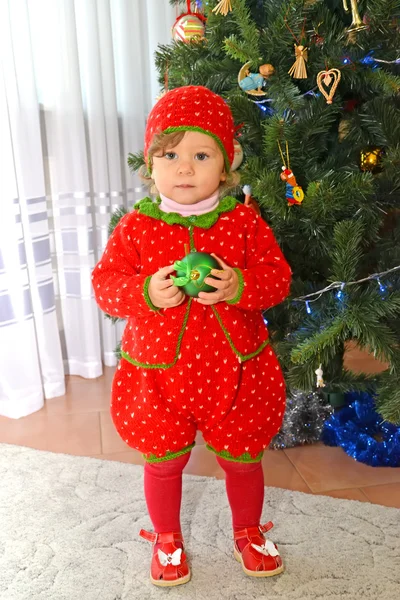 La niña de un año con un traje de fresa está cerca de un árbol de Año Nuevo — Foto de Stock