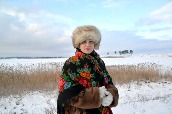 Женщина средних лет в меховой шапке и разноцветной шале стоит на берегу зимнего озера — стоковое фото