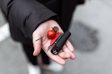 Çocuk elinde çakmak kullanarak birkaç fişek yakıyor. Çocuk havai fişeklerle ya da havai fişeklerle kutlamaya hazırlanıyor. Elinde bir petard tutan bir çocuk. Yakın çekim.