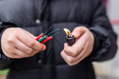Çocuk elinde çakmak kullanarak birkaç fişek yakıyor. Çocuk havai fişeklerle ya da havai fişeklerle kutlamaya hazırlanıyor. Elinde yanan bir patlayıcıyı tutan bir çocuk. Yakın çekim.