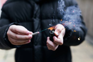 Elindeki kestane fişeği. Elinde yanan bir patlayıcıyı tutan bir çocuk. Havai fişekleri olan bir çocuk dışarıda kıvılcımlar saçar ve sigara içerdi. Havai fişek ve çakmak elinde..