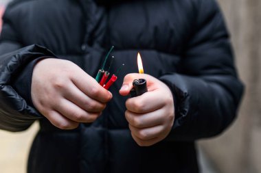 Çocuk elinde çakmak kullanarak birkaç fişek yakıyor. Çocuk havai fişeklerle ya da havai fişeklerle kutlamaya hazırlanıyor. Elinde yanan bir patlayıcıyı tutan bir çocuk. Yakın çekim.