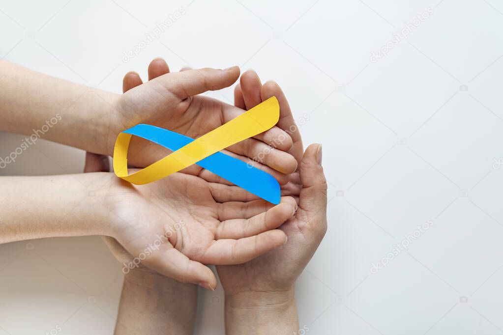 Blue yellow awareness ribbon on helping hand for World down syndrome day WDSD March 21 raising support on patient with down syndrome illness disability and Thoracic Outlet Syndrome - (TOS)