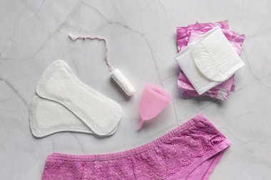 Hijyenik peçeteli pembe pantolon, tampon, beyaz arka planda regl kupası. Kritik günler kavramı, adet görme