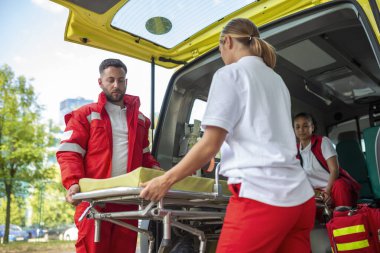 Ambulansın yanında sedye taşıyan sağlık görevlileri. Sağlık görevlileri ambulans arabasını sedyeyle çıkarıyorlar.