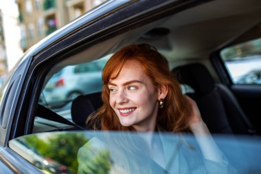 Gülümseyen Kızıl Saçlı Kadın Arabadan Dışarı Bakıyor, Manzaranın tadını çıkaran Mutlu Kadın Yolcu, Arabayla Yolculuk eden Genç Kızıl Kız, Modern Yaşam Tarzı ve Ulaşım Konsepti.