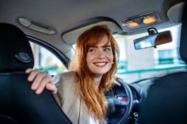 Mutlu Kızıl Saçlı Kadın Araba Kullanıyor ve Gülümsüyor, Neşeli Kadın Sürücü Ters Aracı, Genç Profesyonel Kadın İşe Dönüş, Modern Otomotiv Yaşam Tarzı.