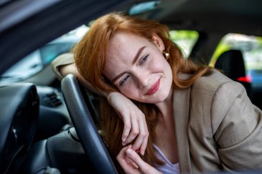 Güzel kızıl saçlı kadın direksiyona yaslanıyor, kameraya bakan rahat kadın sürücü, araçtaki genç kızıl kadın portresi, otantik yaşam tarzı ve seyahat konsepti..