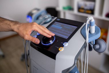 Modern bir fizik tedavi ve rehabilitasyon makinesinin kontrol düğmesini profesyonel bir klinik ortamda dijital ekran ve tıbbi sensörlerle ayarlayan bir insan eli.