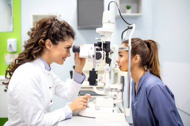 Oftalmolog, yarık lambayla hastayı muayene ediyor. Modern optometri kliniğinde ya da hastanede görme testi ve tanı taraması yapan profesyonel kadın doktor..