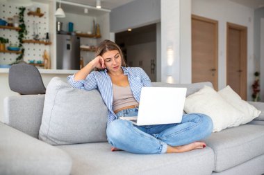 Evde dizüstü bilgisayarla çalışan bir kadın. Uzaktan çalışma ve serbest çalışma kavramı. Çekici genç bir bayan bilgisayar kullanarak kanepede oturuyor. Modern yaşam tarzı, eğitim ve dijital göçebe oturma odasında çalışıyor..