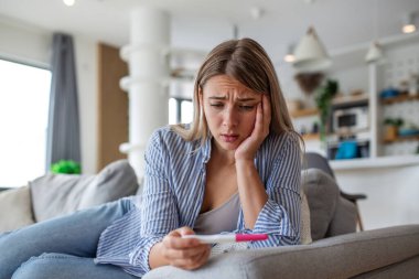 Hamilelik testi tutan üzgün bir kadın. İstenmeyen hamilelik ya da kısırlık kavramı. Sağlık ve yaşam sorunları olan insanlar. Kanepede oturan çekici sarışın kadın hamilelik sonuçlarına bakıyor..