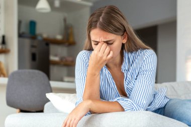 Gözlerinde ağrı var. Görme sorunu ve baş ağrısı, sağlık sorunları olan insanlar, sağlık hizmetleri ve tıp konsepti. Çekici kadın kanepede oturuyor ve acı dolu burun köprüsünü kapalı gözlerle tutuyor..