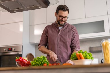Günlük gömlekli, mutfak adasında taze sebze doğrayan, erkek yetişkin, sağlıklı salatayı kiraz domatesli, marullu, modern mutfak içi ve sağlıklı beslenme konseptiyle hazırlayan adam..