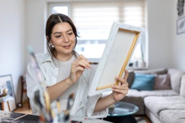 Ev stüdyosundaki küçük bir tuval resmine ince detaylar uygulamaya odaklanmış kadın sanatçı. Parlak, modern bir dairede fırçayla çalışan yaratıcı bir kadın. Sanatsal süreç.