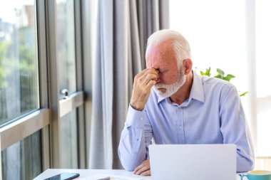 Ofiste göz yorgunluğu çeken yorgun kıdemli işadamı. Çok çalışan yaşlı erkek yönetici burun köprüsüne dokunuyor ve gözleri kapıyor. Dizüstü bilgisayar başında yorgunluk ve tükenmişlik çeken bir profesyonel..