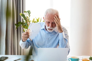 Kıdemli işadamı kendini seksi hissediyor ve ofis masasında vantilatör kullanıyor. Aşırı ısınmış yaşlı bir yönetici dizüstü bilgisayarla çalışırken sıcak çarpması ya da ateşten muzdarip. Menopoz semptomları veya bozuk klima konsepti.