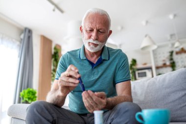 Diyabet yönetimi. Kıdemli adam kan şekeri testi için parmağını delmek için mızrak kullanıyor. Diyabet hastası yaşlı bir erkek evde kan şekeri, sağlık ve tıp konseptini kontrol ediyor..