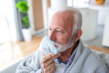 Evde solunum tedavisi için nebulizör kullanan kıdemli bir adam. Astımı olan yaşlı bir erkek hasta ya da solunum terapisi için oksijen maskesi takıyor. Yurt içindeki sağlık ve tıbbi konsept.
