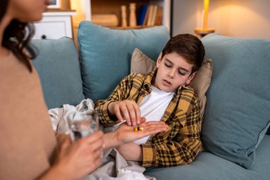 Hasta çocuk ilaç hapı alıyormuş. Çocuk su, sağlık ve tıp konseptiyle kapsülleri elinde tutuyor. Hasta çocuğun tedavi gördüğü ve kanepede grip ve ateş için antibiyotik aldığı hastalara yakın durun..