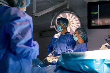 Mavi önlüklü ve yüz maskeli cerrahlar ileri düzey tıbbi ekipman ve monitörlerle minimum invaziv laparoskopik ameliyat yapıyorlar..