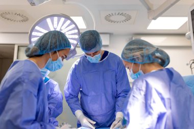 Ameliyathanede bir grup cerrah. Profesyonel Tıbbi Ekip Parlak Lamba altında Cerrahi Prosedür uyguluyor. Doktorlar ve hemşireler birlikte çalışıyor. Sağlık, Tıp ve Cerrahi Birliği Konsepti.