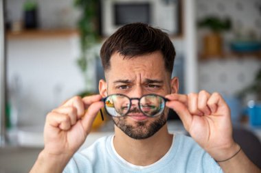 Genç adam, bulanık görüşlü gözlüklerle bakıyor. Erkek Gözlük Tutma ve Evde Görüş Kontrol. Göz Sorunları ve Görme Engelli Kişilerin Sağlık ve Tıp Konsepti.