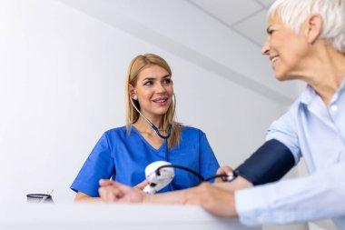 Klinikteki hasta danışmanlığı. Steteskoplu kadın doktor tansiyon testi sırasında yaşlı kadınla konuşuyor. Sağlık ve tıp konsepti, tıbbi profesyonel sağlık kontrolü.