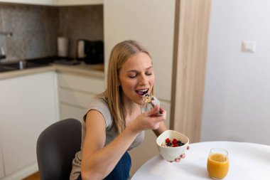 Mutfak, Sağlık ve Beslenme Konsepti 'nde Sağlıklı Kahvaltı Kâsesi' nin keyfini çıkaran Mutlu Kadın. Çekici sarışın kadın taze böğürtlenli yulaf ezmesi yiyor ve sabah rutininde portakal suyu içiyor..