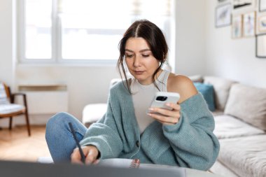 Dahili ofiste planlama yaparken akıllı telefon kullanan kadın profesyonel. İş kadını mobil cihaz ve not defteriyle birden fazla iş yapıyor. Organizasyon ve uzak yönetim kavramı.