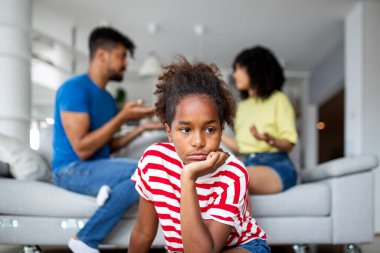 Ebeveynler arka planda kavga ederken dalgın bir Afrikalı Amerikalı çocuk dinleniyor. Aile içi çatışma, çocukluk endişesi, aile sorunları ve ebeveynliğin duygusal bedeli.