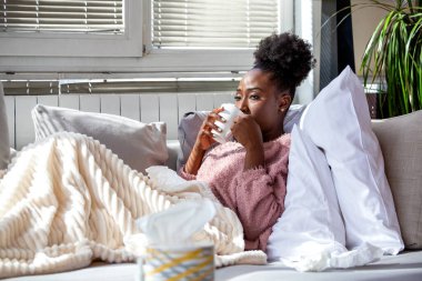 Grip belirtilerinden kurtuldum. Çay içen hasta Afro-Amerikan kadın mevsimsel hastalık sorunu olan insanlar, Sağlık ve Tıp konsepti. Yorgun, siyah bir kadın kanepede dinleniyor..