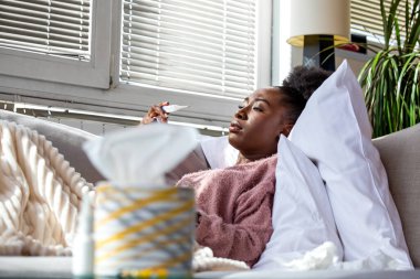 Vücut ısısını kontrol ediyorum. Ateşli hasta Afrikalı Amerikalı kadın, grip ve virüs sorunu olan insanlar, Sağlık ve Tıp Konsepti. Kanepenin üzerinde dijital termometre tutan siyah bir kadın var..