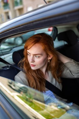 Genç kızıl saçlı kadın arabanın arka koltuğunda oturmuş pencereden dışarı bakıyor. Zencefilli kız taksi ile seyahat ediyor ya da şehirde at paylaşımı yapıyor. Ulaşım ve şehir yaşam tarzı konsepti. Doğru alıcı odaklandı.