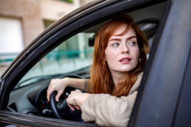 Odaklanmış kadın sürücü araçta otururken trafiği gözlemliyor. Yol güvenliği için profesyonel imaj, sürücü farkındalığı, araba sigortası yükümlülüğü ve kentsel ulaşım navigasyonu.