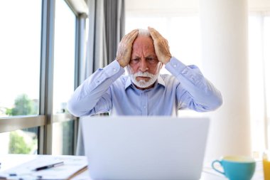 Hüsrana uğramış kıdemli işadamı, bilgisayar ekranına bakarken kafasını iki eliyle tutuyor. İş yerinde tükenme, stres, migren ve zihinsel sağlık sorunları kavramı.