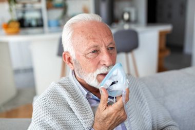 Solunum Terapisi, Sağlık ve Solunum Sorunu Konseptinde Oksijen Maskesi Kullanan Yaşlı Adam. Kapalı bir koltukta otururken gri sakallı, nebulizör maskeli son sınıf erkek hasta..