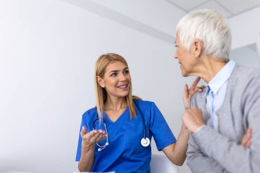 Parlak bir tıp bürosunda rutin bir sağlık kontrolü sırasında yaşlı bir hastaya empatik bakım ve tavsiye veren mavi önlüklü bir kadın doktor..