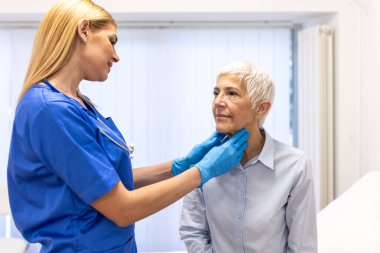 Hemşire, yaşlı hastanın tiroit ve lenf bezlerini kontrol ediyor. Sağlık ve tıp konsepti. Tıbbi konsültasyon ve sağlık kontrolü sırasında yaşlı bir kadının boynunu muayene eden kadın doktor..