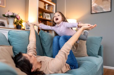 Anne kanepede kızıyla uçak oyunu oynuyor. Aile eğlencesi, çocuk gelişimi ve bağlanma konsepti. Kanepede uzanmış, küçük kızı kaldıran bir kadın..