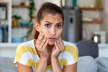 Diş Ağrısı, Yüze Dokunan Genç Kadın, Diş Sağlığı Sorunları, Diş Sağlığı Sorunları, Sağlık ve Tıp Konsepti. Çekici bir kadın kanepede oturuyor ve elleriyle acı dolu yanaklarını tutuyor.