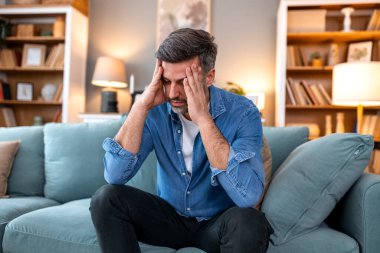 Baş ağrısı ve migren gerilimi strese bağlı sorunları olan insanlar, Sağlık ve Tıp Konsepti. Kanepede oturan ve iki eliyle alnını tutan bir adam. Kronik yorgunluktan muzdarip.