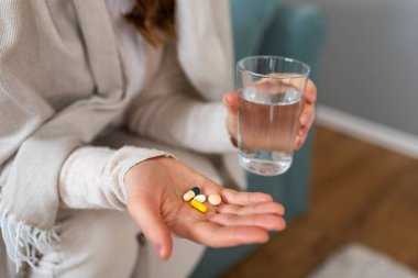 İlaç alıyorum. Haplarla, sağlık sorunları olan insanlarla, sağlık hizmetleri ve tıp konseptiyle ilgilenin. Kadın bir bardak su ve çeşitli renkli kapsüller ve tabletleri açık avuç içinde tutuyor..