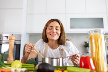 Yemeğin kokusunu alıyorum. Mutfakta nefis bir koku, yemek kokusundan hoşlanan bir kadın sağlıklı yemek ve beslenme konsepti. Çekici, gözleri kapalı bir kadın taze sebzeli bir çorba tenceresinin üzerine eğilmiş..