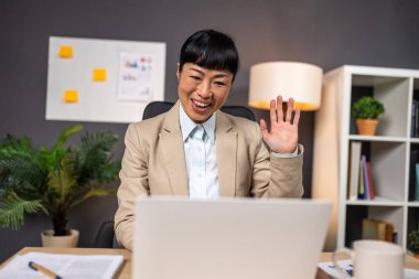 Laptop Video 'da mutlu Asyalı iş kadını el sallaması. Çevrimiçi Buluşmada Profesyonel Kadın İş Arkadaşlarını Karşılıyor. Ofiste Olgun Kadın Yönetici. Uzak Çalışma ve Sanal Bağlantı Konsepti.