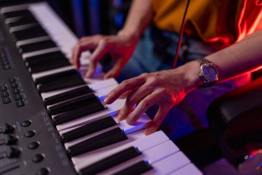 Eller dijital piyano klavyesi çalıyor. Müzisyen ev stüdyosunda müzik yaratıyor, Sanat ve Eğlence konsepti. Kadın ellerinin piyano tuşlarına yakın plan mavi ve kırmızı profesyonel ışıklandırma ile.