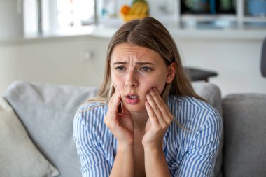 Diş ağrısı ve diş problemi. Çekici bir kadın elleriyle çenesini tutuyor ve acı çekiyor. Sağlık ve tıp konsepti. Kanepede oturan kız hassas dişler ya da diş eti iltihabından muzdarip..