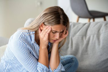 Şiddetli migren ağrısı çeken bir kadın. Gerilim Baş Ağrısı, Sağlık ve Tıp Konsepti. Kanepede oturan ve elleriyle acı çeken genç bir kadın. Hüsrana uğramış kız kendini kötü hissediyor..