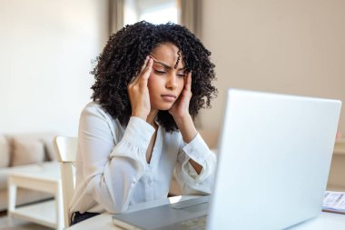 İş sırasında baş ağrısı. Migren ve stres, kas problemi olan insanlar, sağlık ve ilaç konsepti. Çekici bir kadın masada oturuyor, dizüstü bilgisayarını kullanırken şakaklarını elleriyle tutuyor..