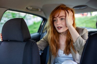 Stresli kızıl saçlı kadın arabanın arka koltuğunda şaşkın şaşkın oturuyor. Kızıl saçlı, takside kafasına dokunan kadın yolcu şok oldu. Kötü haber, stres, endişe ve araçtaki beklenmedik durum konsepti.